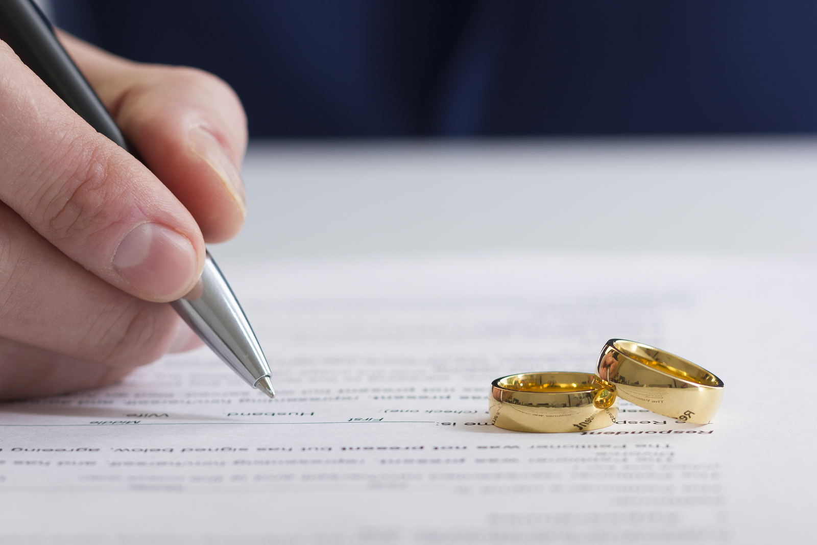 hand of person signing document with wedding rings lying on it